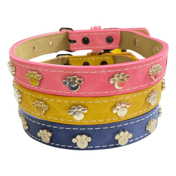 Collares para perro en colores rosa, mostaza y azul decorados con huellitas metálicas, apilados para mostrar diseño y textura
